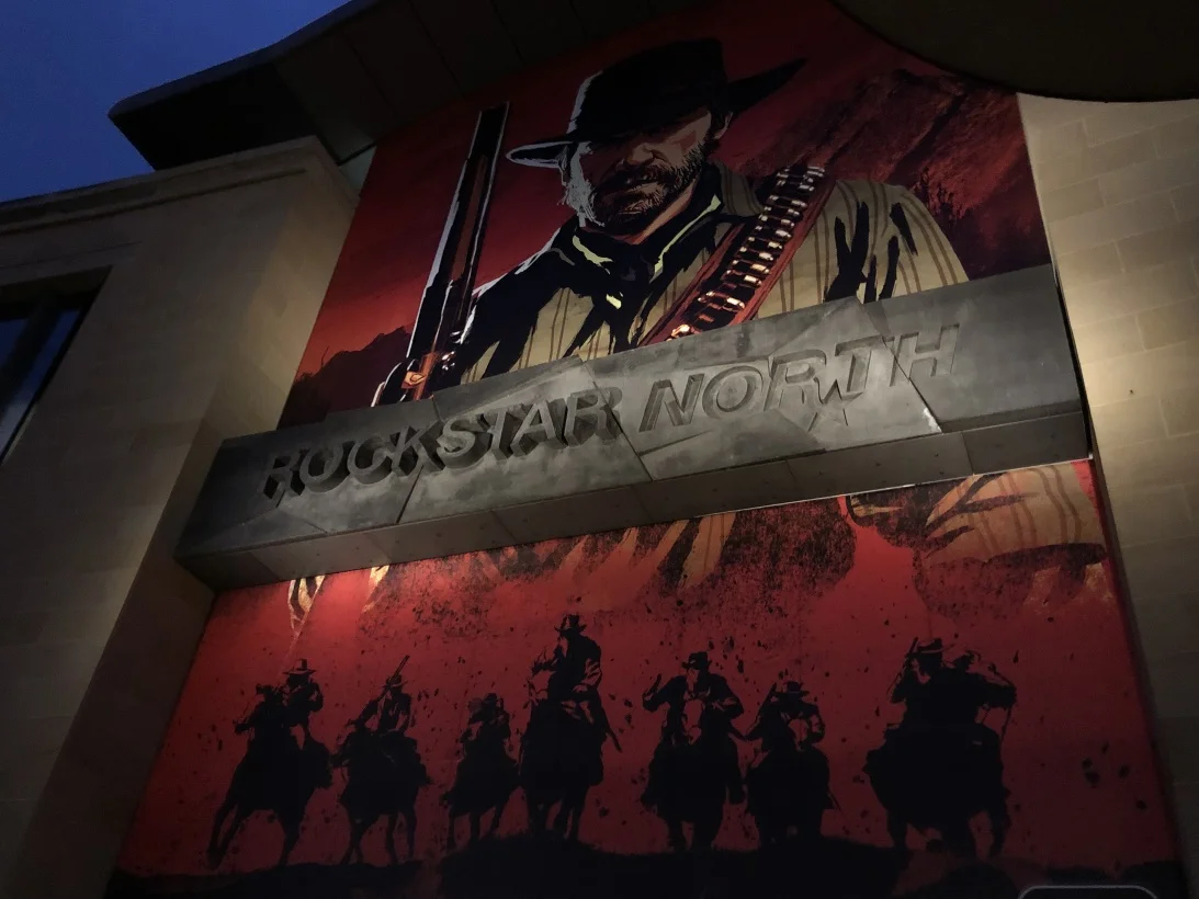 Building Facade with a Large Poster of a Cowboy Gunfighter Above a Metal Sign Reading 'rockstar North' Plus Silhouettes of Riders on a Red Backdrop Beneath